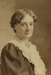 Early 20th century white woman with short hair, dark dress elaborate white lace collar 